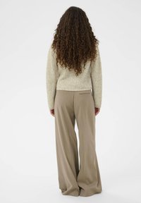 Svijetlosmeđi pleteni pulover s skraćenim rubom, uparen s širokim taupe hlačama koje imaju jedan stražnji džep.