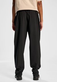 Czarne spodnie o luźnym kroju, z elastycznym paskiem w talii, bocznymi kieszeniami oraz gładkim, lekkim materiałem. Widoczne detale szwów.
