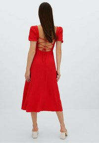 Czerwona sukienka średniej długości z bufiastymi rękawami, teksturowanym materiałem i krzyżującym się wzorem na plecach. Gładka spódnica rozszerza się od talii.