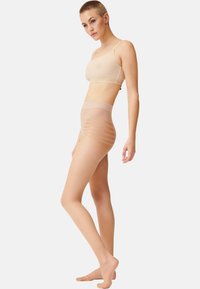 Bralette senza cuciture e collant a vita alta in colore nude, realizzati in materiale morbido e trasparente. I collant presentano un motivo a strisce orizzontali lungo le gambe.