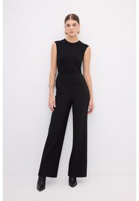 Haut sans manches noir associé à un pantalon large noir taille haute. Tissu lisse, design minimaliste, accessoirisé avec des boucles d'oreilles créoles dorées.