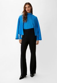 Blauer Blazer über einem passenden Rollkragenpullover, kombiniert mit schwarzen Glockenhosen. Der Blazer verfügt über abgerundete Revers und eine lässige Passform.