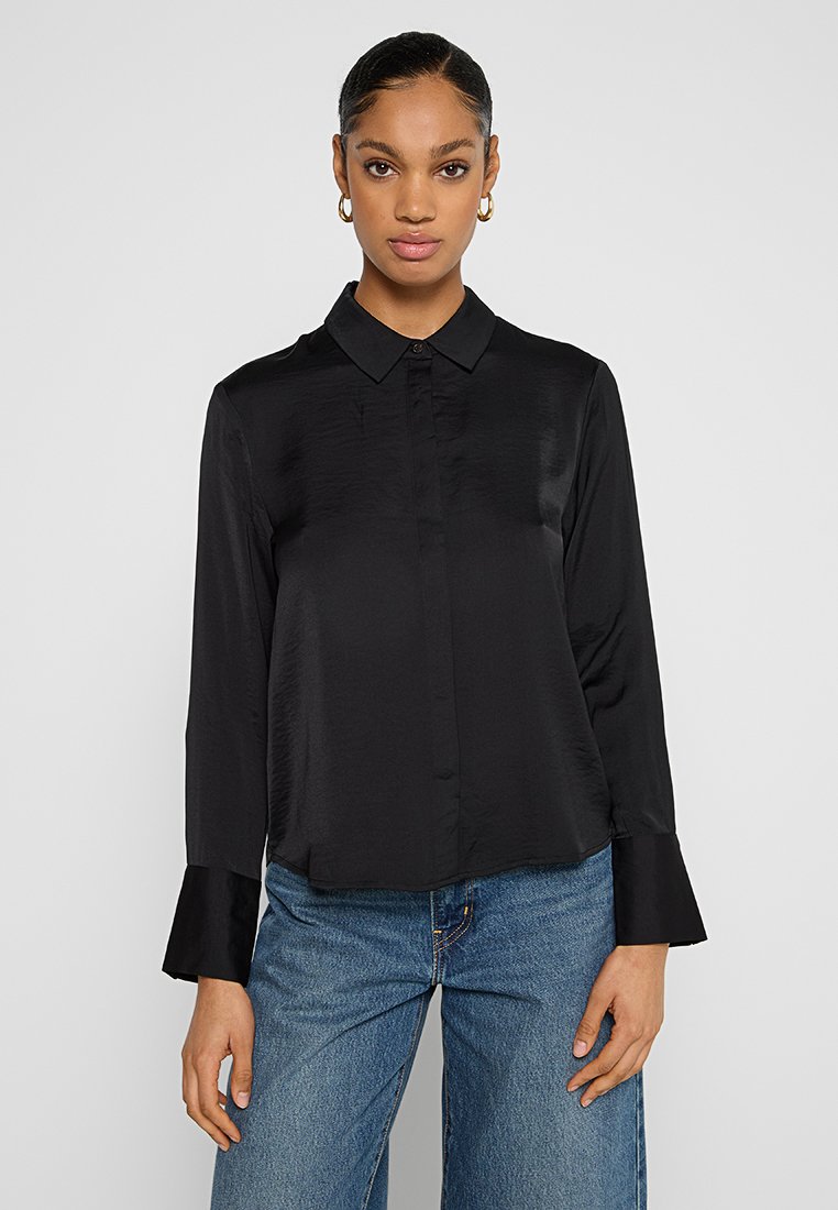 Zwarte blouse van gladde stof, met een klassieke kraag, knoopsluiting aan de voorkant en lange mouwen met een licht uitlopende manchet.