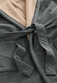 Hallhalli struktuuriga hall vannitoot, millel on vahvlitükk, pehme beež vooder ja seotud vöö, mis on loodud mugavuseks ja soojuseks.