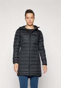 Zwarte pufferjas met capuchon, voorzien van een verticale gestikte patroon en een rits aan de voorkant; gecombineerd met blauwe leggings, minimalistisch ontwerp en aansluitende pasvorm.