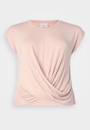 Haut rose clair à manches courtes avec un col rond. Présente un tissu froncé à l'avant et sur les côtés pour un effet drapé. Matière douce et extensible.