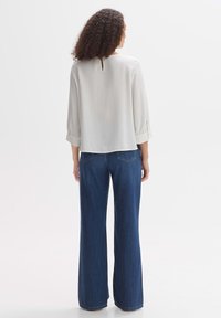 Blouse blanche légère avec des manches trois-quarts et un décolleté en trou de serrure au dos. Associée à un pantalon en denim bleu à jambes larges avec une texture classique.