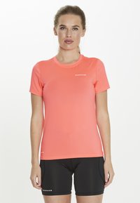 Women's short-sleeve top in bright coral, made from stretchy, lightweight fabric; paired with black shorts featuring a logo accent.