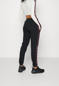 Joggers negros con franjas laterales rosas, fabricados con material suave. Cuentan con piernas ajustadas y una cinturilla elástica, combinados con zapatillas deportivas negras.