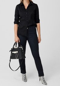 Schwarzes Hemd mit Knöpfen, dunkle Jeans und graue Schlangenleder-Stiefeletten. Schwarze Handtasche mit weißen Akzenten und Kettendetails.