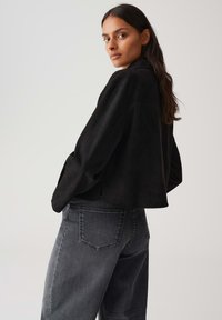 Giubbotto in suede nero con un design corto, caratterizzato da maniche larghe, abbinato a jeans grigi sbiaditi a vita alta con tasche posteriori.
