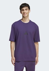 Violet medvilninis marškinėliai, kuriuose trumpi rankoviai, apvalus kaklas ir juodas Adidas logotipas priekyje. Lygus paviršius, laisvas siluetas.