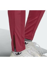 Dopasowane sportowe spodnie w jaskrawym czerwonym kolorze z bocznymi zamkami błyskawicznymi, w połączeniu z białymi sneakerami i czarno-białymi skarpetkami w paski.