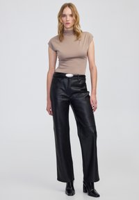 Obcisła beżowa bluzka z golfem zestawiona z czarnymi, skórzanymi spodniami o wysokim stanie i szerokimi nogawkami oraz czarnymi, skórzanymi botkami na obcasie.