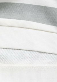 Un tessuto bianco presenta un motivo a maglia testurizzato, arricchito da una striscia grigia liscia che attraversa la larghezza. I bordi sono rifiniti con cuciture ordinate.