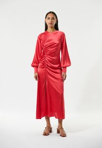 Rotes Satinkleid mit langen Puffärmeln, ausgestattet mit gerafften Details an der Taille und einem Schlitz vorne. Glatte Textur und mittellanges Design.
