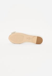 Chaussure blanche avec une tige lisse et une semelle en caoutchouc texturée. Les détails notables incluent une semelle intérieure à motifs et un accent beige sur le talon.