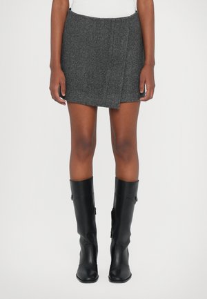 Jupe enveloppante en tweed gris avec une coupe diagonale, associée à des bottes en cuir noires arrivant au genou. La jupe a un fini texturé et un motif subtil.
