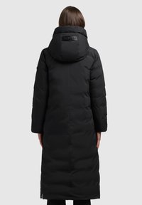 Lang sort puffet jakke med hætte, der har et blankt logo på ryggen, quiltet tekstur og sidelommer med lynlås. Glat stoffinish.