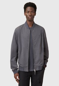 Giacca bomber grigia realizzata in tessuto liscio, con chiusura con zip, polsini e orlo a costine, e un logo sottile sul petto.