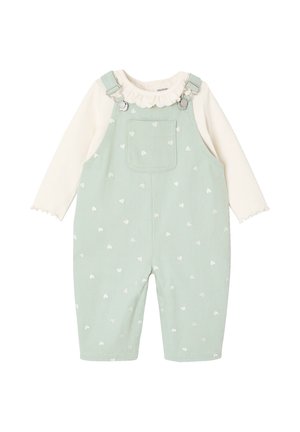Baby-Latzhose in Minzgrün mit weißen Herzmustern über einem cremefarbenen Langarmshirt mit Rüschenkragen und Manschetten.