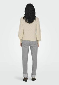 Suéter de punto en crema con un patrón de diamante, mangas abullonadas, usado sobre jeans rectos grises con dobladillos y zapatos oscuros.