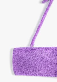 Bolso de mano púrpura de tela con un patrón texturizado en zigzag, que cuenta con una correa delgada para llevar. El diseño es rectangular con un acabado fruncido.