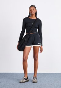 Čierny rebrovaný dlhý rukáv crop top, čierne kraťasy s bielym lemovaním, čierna textúrovaná ramenná taška a čierno-biele pruhované topánky.