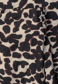 Tissu avec un motif léopard irrégulier noir et brun foncé sur un fond beige clair, montrant des détails pliés et cousus.