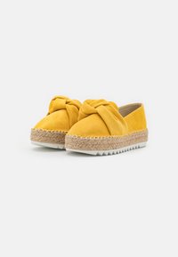 Scarpe slip-on in suede giallo con dettaglio annodato, suola avvolta in juta e suola in gomma bianca a zigzag per una buona aderenza.