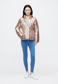 Metallinen ruusukultainen toppatakki, jossa vetoketjullinen etuosa, yhdistetty sinisiin leggingsseihin ja valkoisiin lenkkareihin, joissa on pystysuora tikattu kuvio.