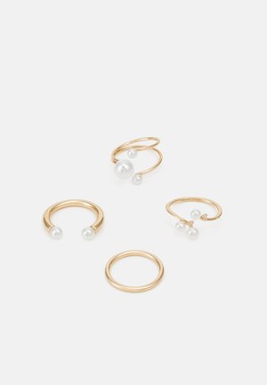 Quatre anneaux en métal doré, dont deux avec des perles blanches. Un anneau a un simple bandeau, et un autre présente un design en spirale avec des perles.