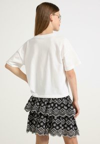 Vit bomulls t-shirt med korta ärmar, kombinerad med en svart volangkjol som har intrikata vita blommönster och scallopade kanter.