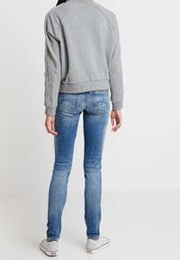 Felpa grigia con orlo e polsini a costine, abbinata a jeans slim-fit blu con leggeri segni di scolorimento. Nessun motivo o accento particolare.