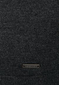 Tessuto nero lavorato a maglia con una fine texture, con un piccolo etichetta metallica vicino al fondo con il marchio.