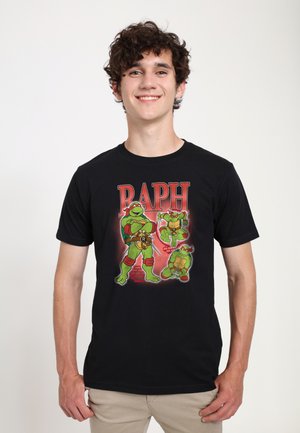 Ung mand, der smiler, iført en sort T-shirt med tre tegneserie Teenage Mutant Ninja Turtles-figurer og teksten "RAPH" i rødt.