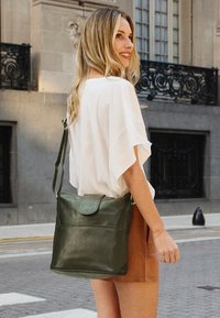 Borsa a spalla in pelle verde con una forma strutturata, chiusura con patta e tracolla regolabile. Tessuto liscio e dettaglio con tasca frontale.