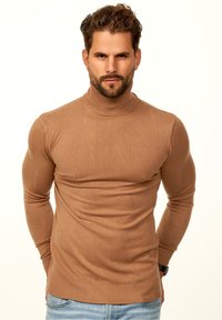 Brauner Rollkragenpullover aus weichem Strickstoff, figurnaher Schnitt, gerippter Ausschnitt und Bündchen, kombiniert mit hellblauen Jeans.
