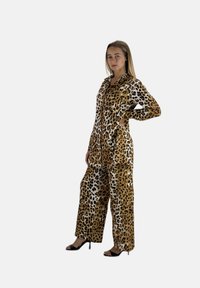 Mono con estampado de leopardo en tonos marrón y crema, con cierre frontal de cremallera, mangas largas y pantalones de pierna ancha. Textura suave, ajuste relajado.