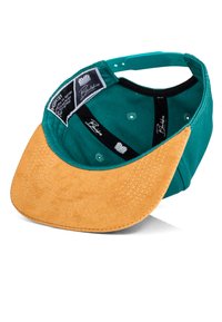 Gorra de tela verde con visera de ante color marrón claro, que presenta etiquetas de marca en el interior y orificios de ventilación. La visera está cosida con múltiples líneas para mayor detalle.