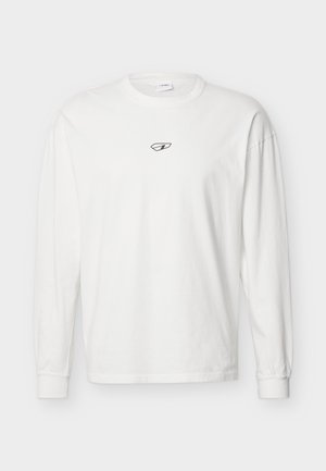 Balti ilgomis rankovėmis marškinėliai su juodu abstrakčiu mažu logotipu krūtinės centre, pateikti ant šviesios fono.