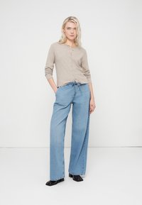 Beige long-sleeve button-up top with a rounded neckline; paired with light blue wide-leg jeans featuring an elastic drawstring waistband.