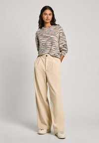 Multicolored textured sweater with a crew neck, paired with cream wide-leg pants featuring front pleats and a button closure, worn with white sneakers.