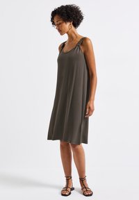 Oliwkowa, bezrękawnikowa sukienka wykonana z miękkiego materiału, z zebranymi ramiączkami i luźnym, swobodnym krojem sięgającym do połowy łydki.