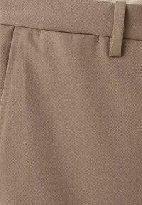 Tessuto intrecciato marrone chiaro dei pantaloni con frontale piatto, passanti per cintura e superficie strutturata, che dimostra un design classico e su misura.