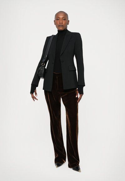 Zwarte op maat gemaakte blazer, aansluitende zwarte coltrui, bruine fluwelen wijde broek en puntige zwarte schoenen met gouden accenten; minimalistisch ontwerp.