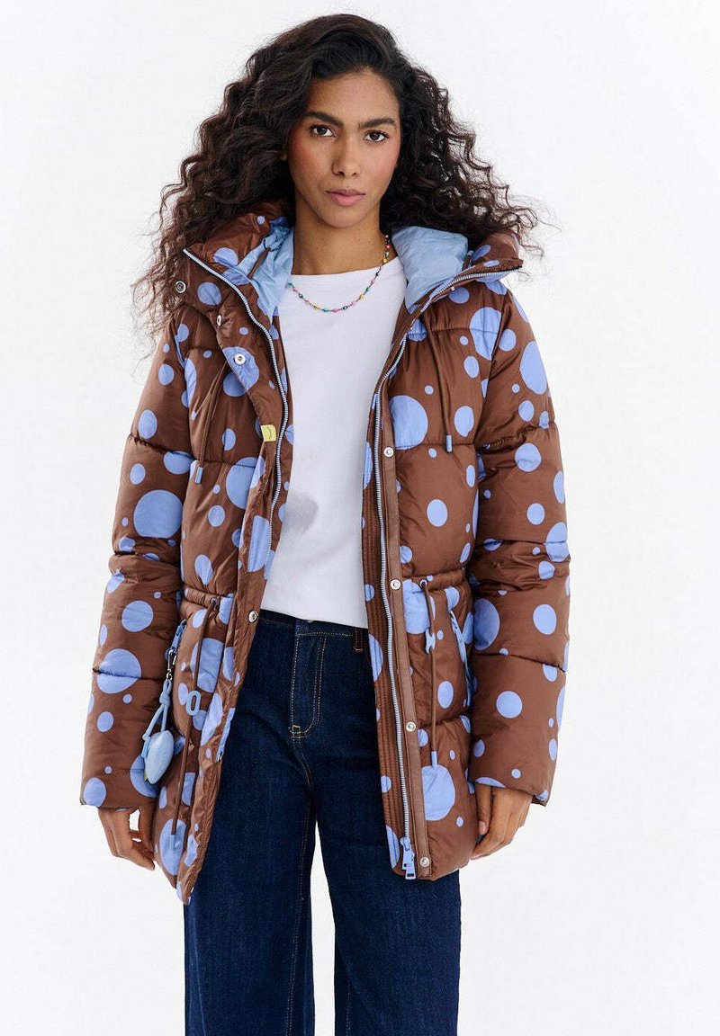 Brązowa kurtka puchowa z dużymi jasnoniebieskimi groszkami, kapturem i przednimi kieszeniami. Posiada zamek błyskawiczny i elastyczne mankiety.