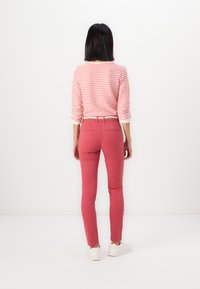 Pantalones ajustados de color rojo-rosado con textura suave y bolsillos traseros, combinados con una camiseta de manga larga a rayas en rosa y blanco.