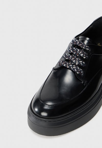 Scarpa in pelle nera con finitura liscia, punta tonda e suola nera spessa. Presenta lacci multicolori texturizzati e cuciture minime.