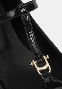 Schwarze Lackleder-Ballerinas mit einem mittleren Riemen, der mit einer goldenen Schnalle akzentuiert ist. Glatte Textur und elegantes Design. Das Innere ist mit schwarzem Material bezogen.